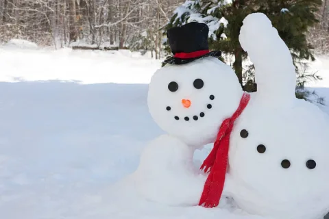Snowman waving as passersby while resting his face on his arm.